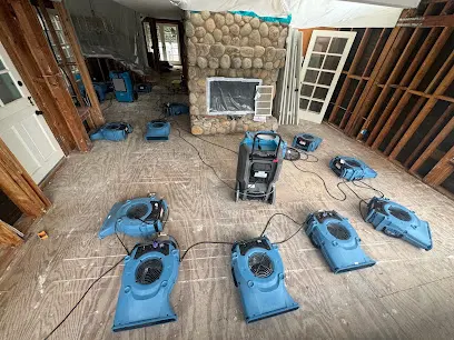 Rows of blue air movers drying a bare subfloor in a room with the walls opened