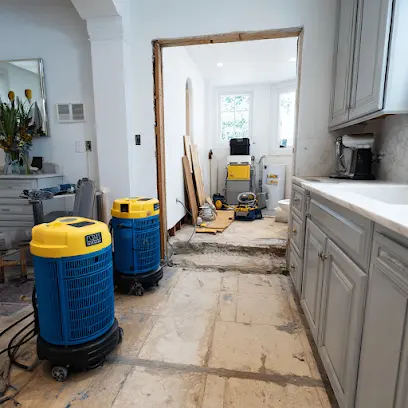 Two dehumidifiers drying a hallway beside kitchen cabinets after the flooring came out