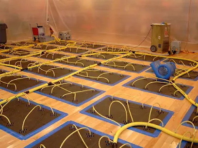 Hardwood floor drying mats with yellow hoses laid in a grid inside plastic containment