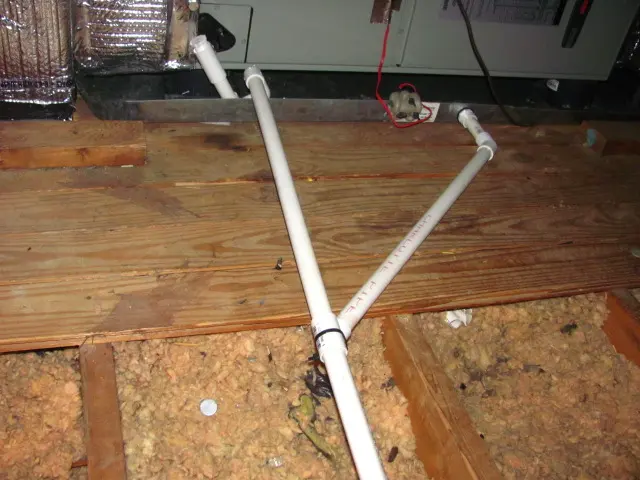 PVC condensate drain pipes running from an air handler across attic boards