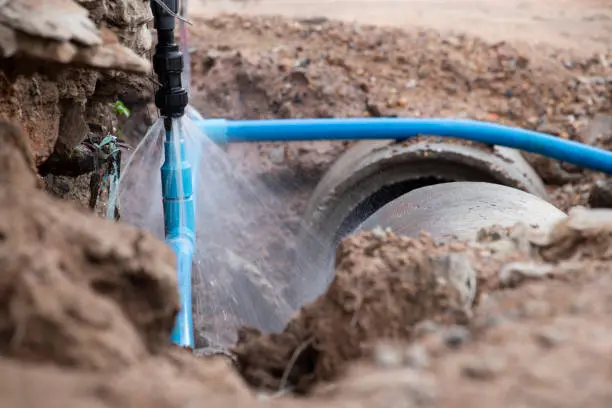 Water spraying from a broken blue water pipe in an open trench