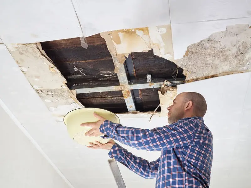 Man holding a bowl under an opened ceiling to catch water leaking from above