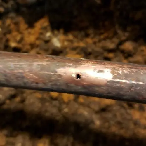 Close view of a small pinhole corroded through a copper water pipe