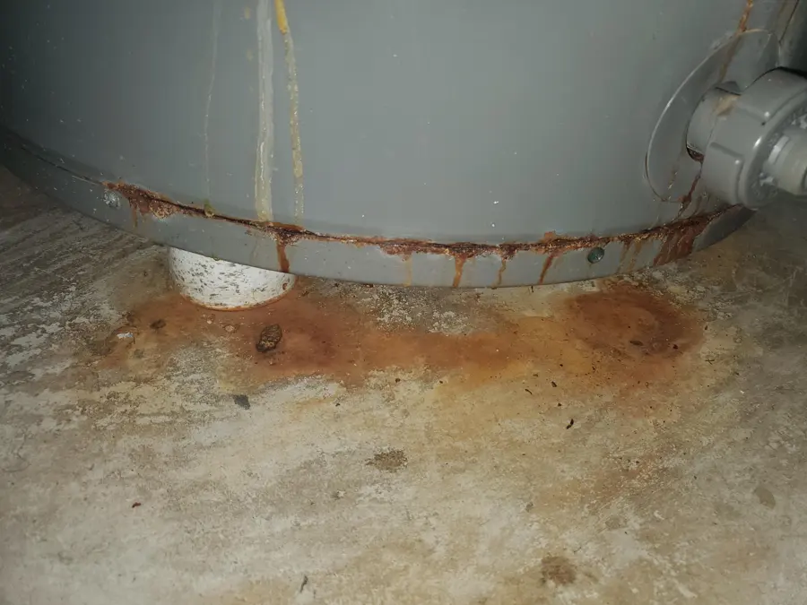 Rusted base of a gas water heater with water and rust stains spreading across the concrete floor